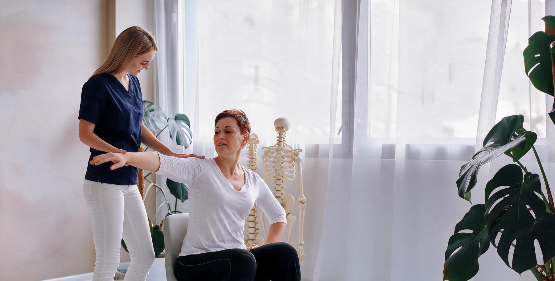 Therapeutin leitet eine Patientin bei einer Schulterübung in der Ordination an