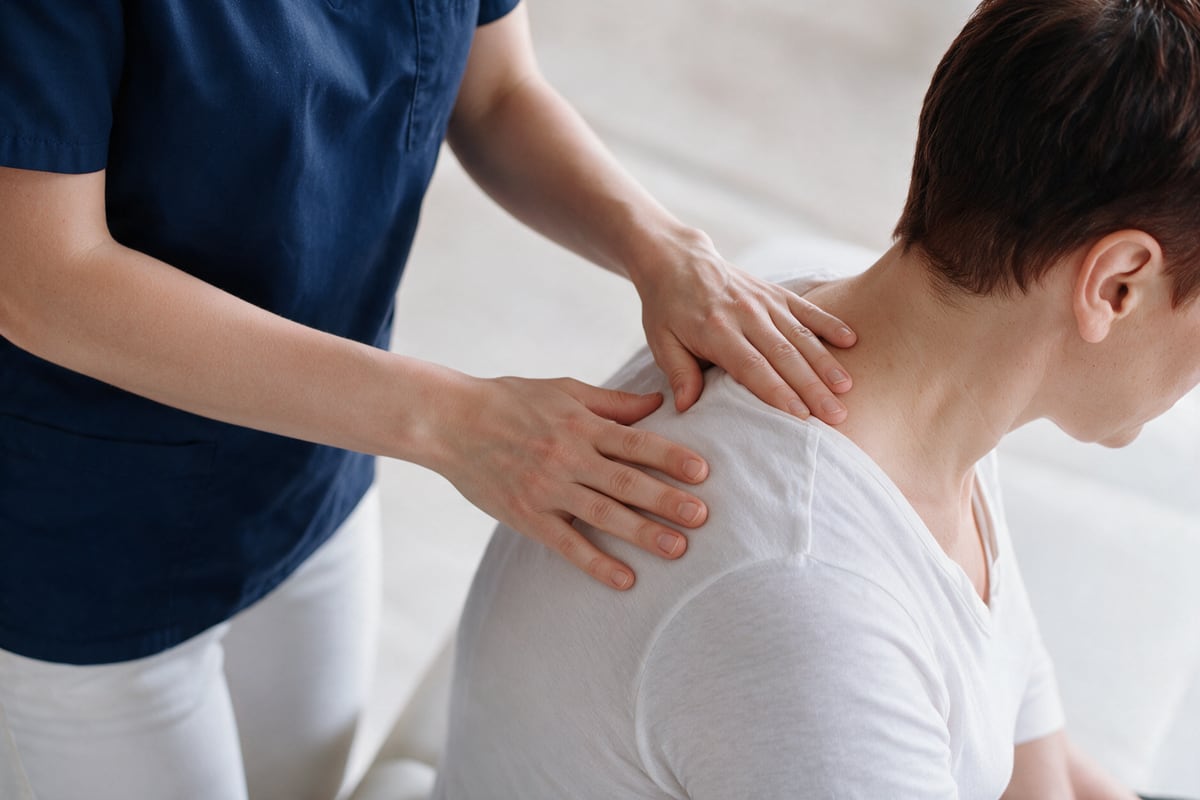 Arzt behandelt die Schulter- und Nackenpartie einer Patientin manuell.