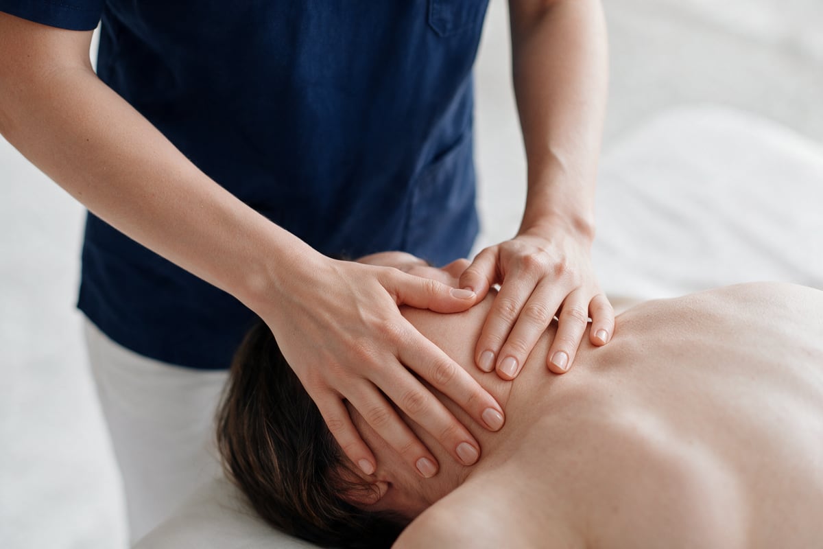 Arzt behandelt die Schulter einer liegenden Patientin osteopathisch.