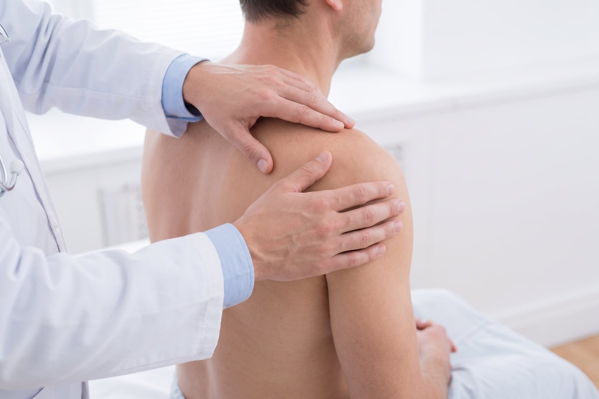 Arzt untersucht die Schulter eines sitzenden Patienten